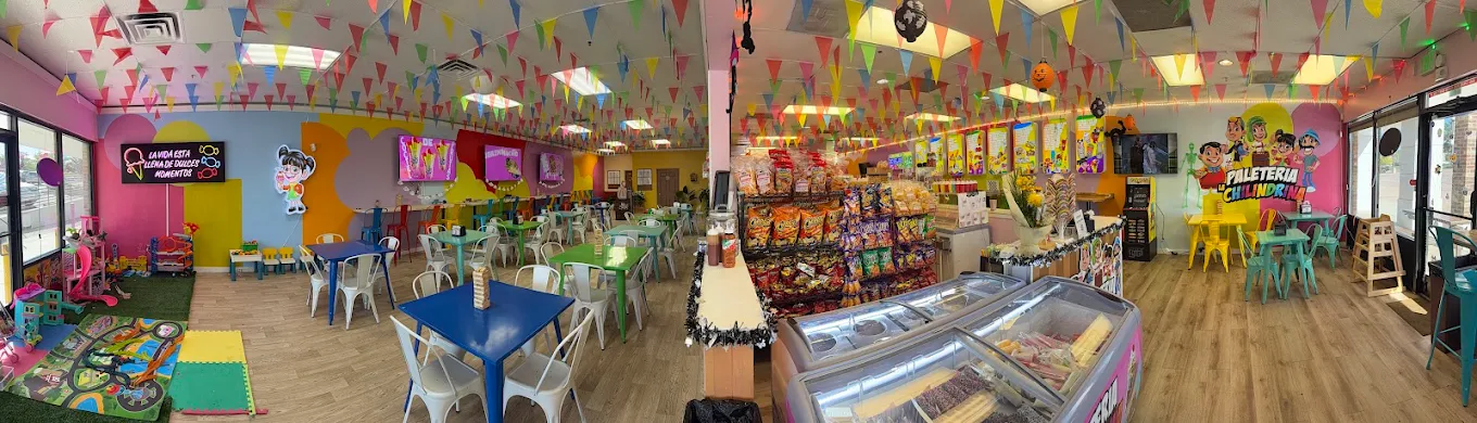 Inside Paleteria La Chilindrina — colorful pennant banners, bright tables and the paleta freezer